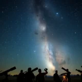 Ciel nocturne rempli d'étoiles avec des astronomes amateurs observant à travers des télescopes.
